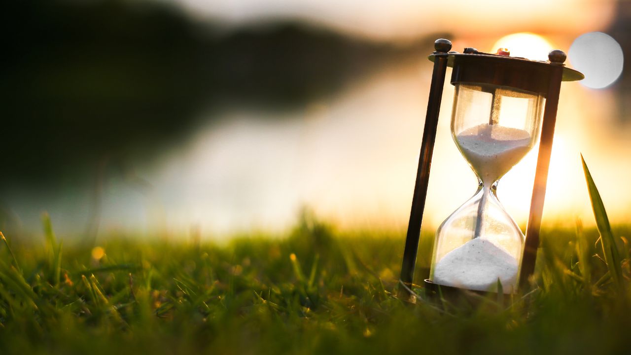 Spirituelle Transformation - Sanduhr mit Lichtpartikeln auf einer Wiese